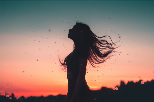 Eine Frau steht mit wehendem Haar im Sonnenuntergang