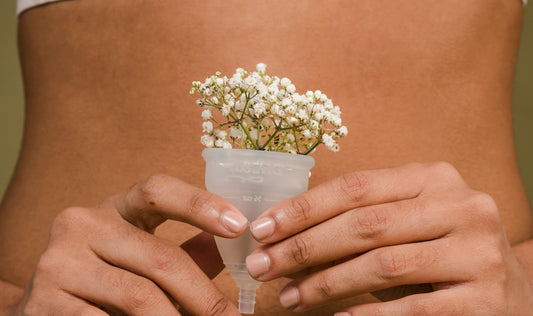 Eine Frau hält eine Menstruationstasse gefüllt mit Blumen vor ihren Bauch