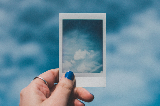 Eine Frau hält ein Polaroidbild, das Wolken am Himmel zeigt
