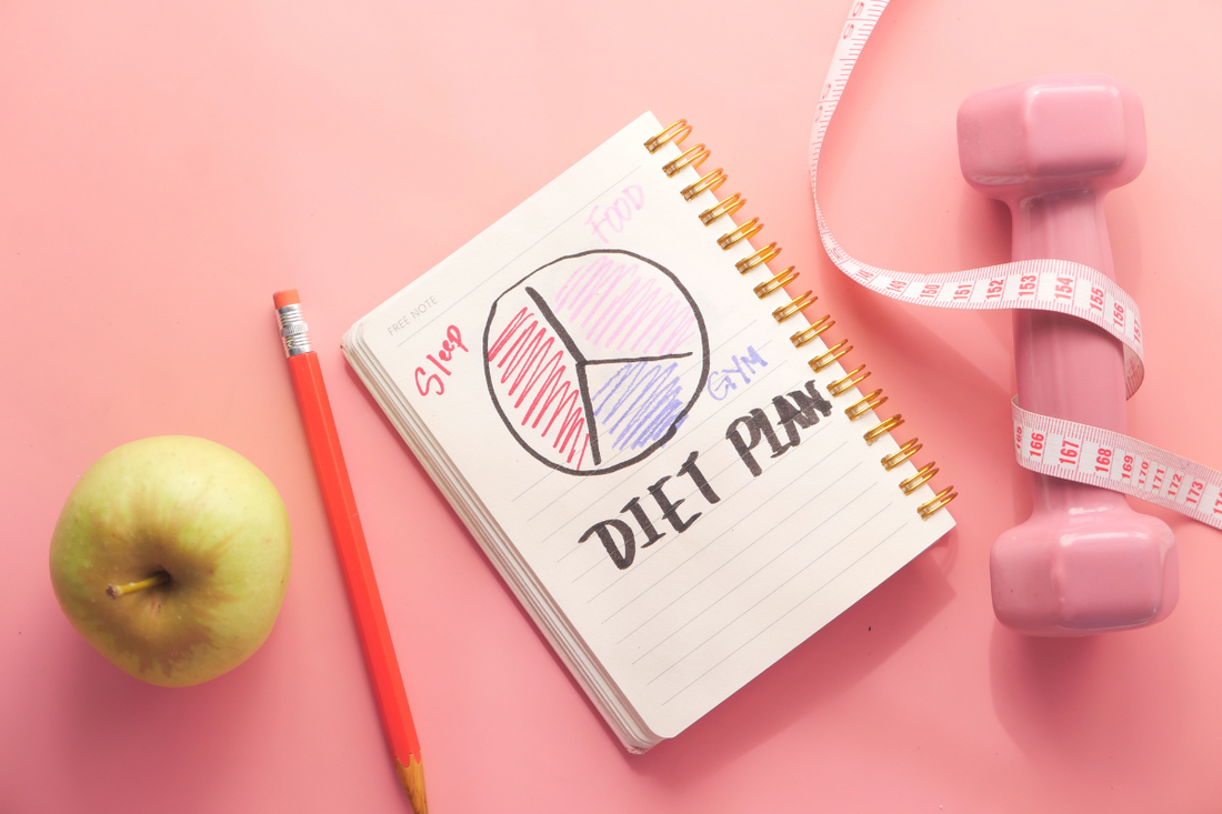 Ein Apfel, ein Diätplan, ein Maßband und eine Hantel liegen nebeneinander